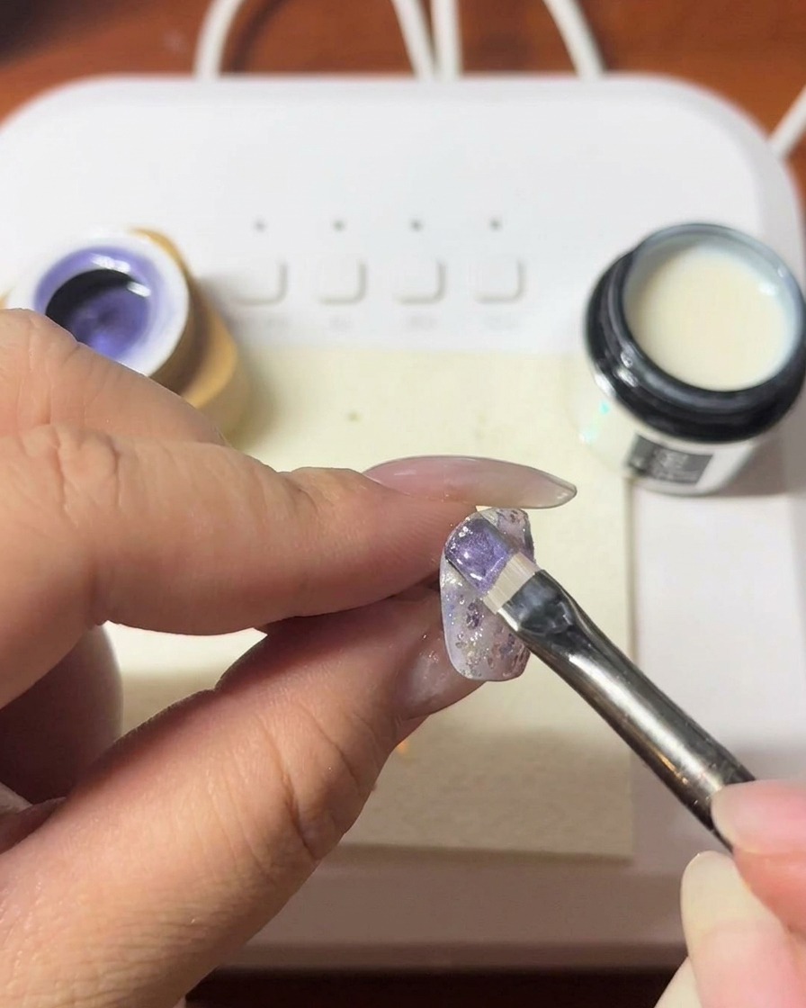 Un aimant tenu près dun ongle pour créer une ligne cat-eye scintillante dans le gel violet.