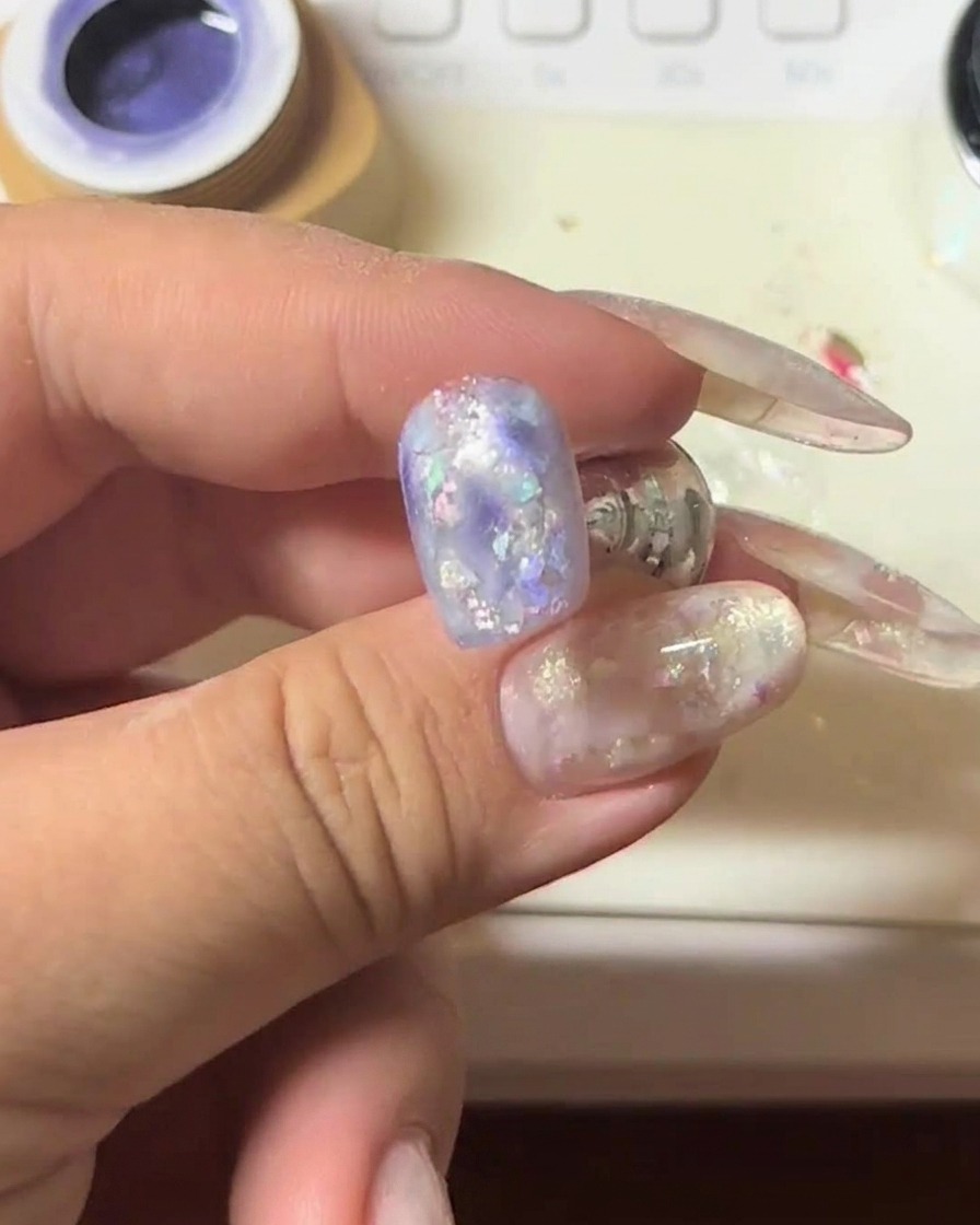 Gros plan dun ongle avec gel cat-eye violet maintenu sous un aimant pour intensifier la bande lumineuse scintillante.