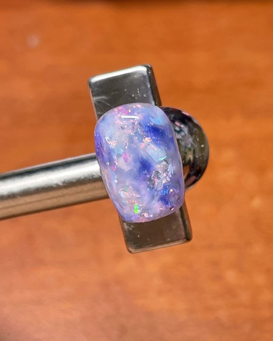 Un pinceau de top coat appliquant une couche finale de scellage sur le nail art fini aux coquillages et paillettes violets.