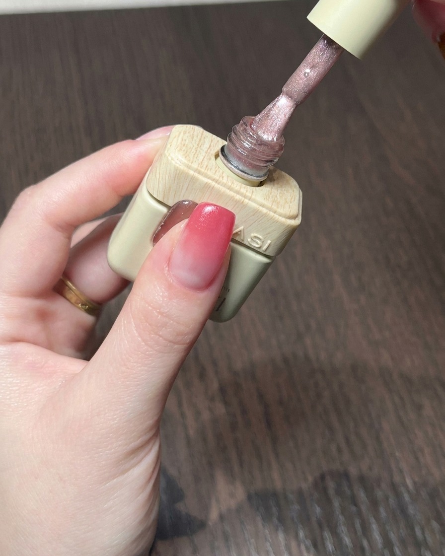 Un pinceau appliquant un gel cat eye nude rosé scintillant sur la base dégradée rouge.