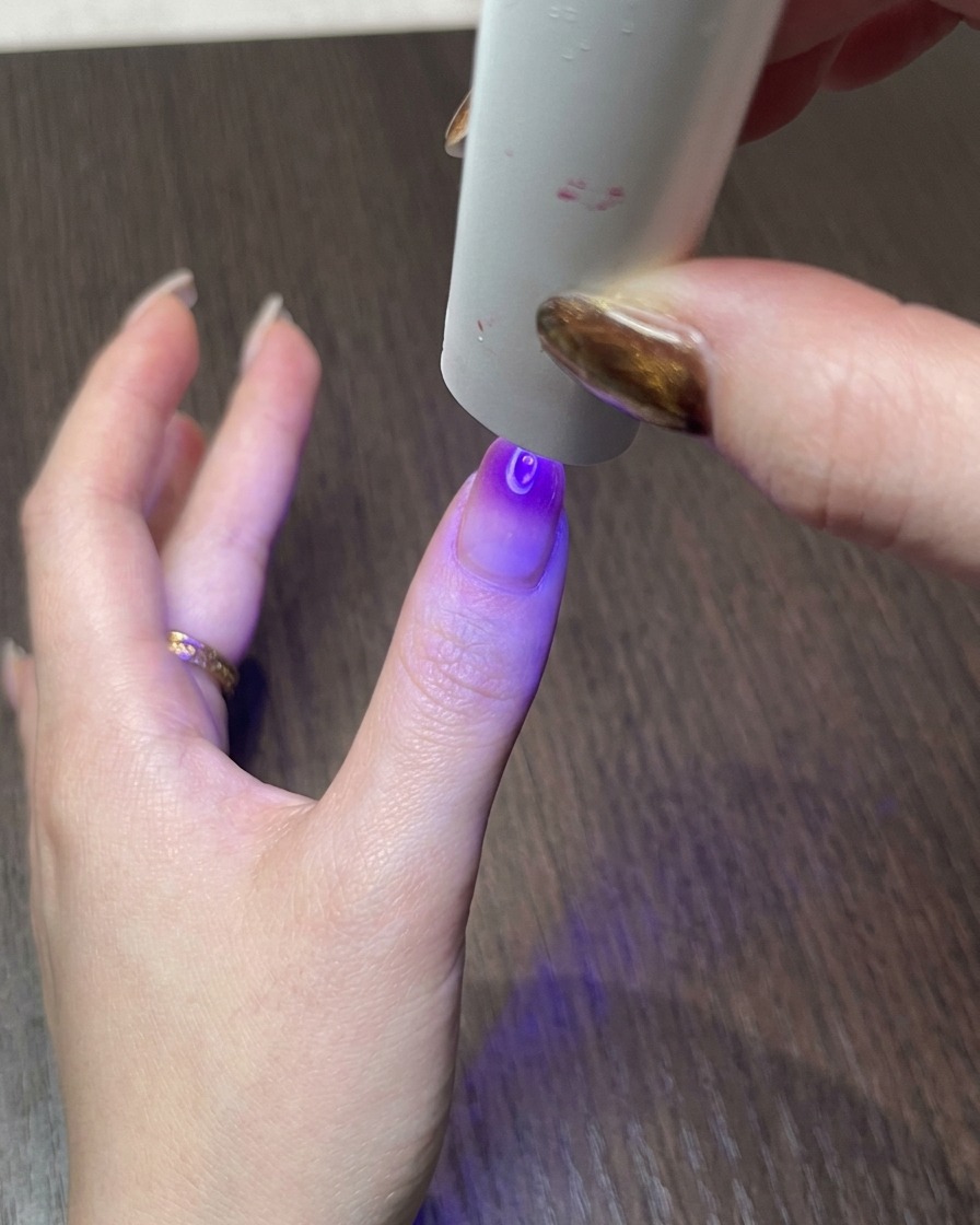 Une main sous une petite lampe UV catalysant le design dongle cat eye magnétique fini.