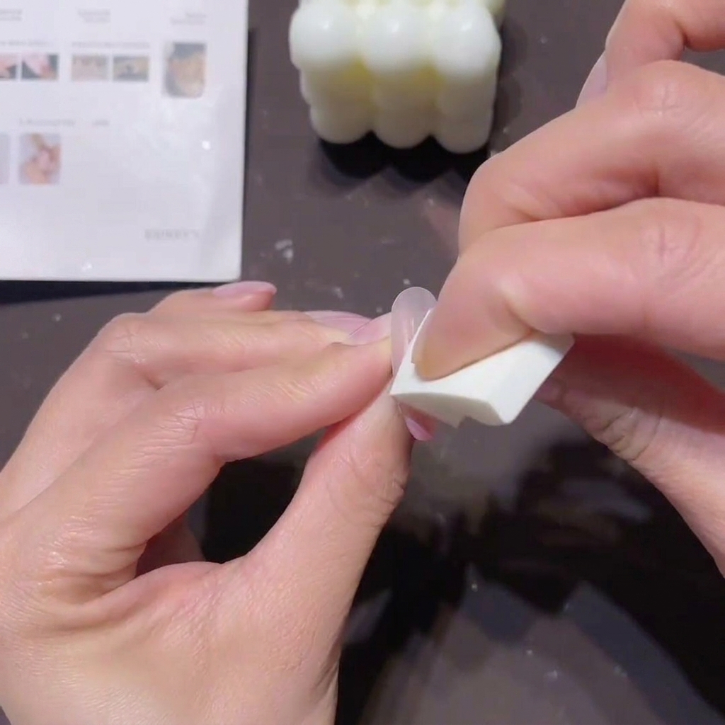 Gros plan des mains dune personne utilisant une petite éponge en mousse blanche pour tamponner du gel pêche-rose sur un ongle afin de créer un effet ombré.