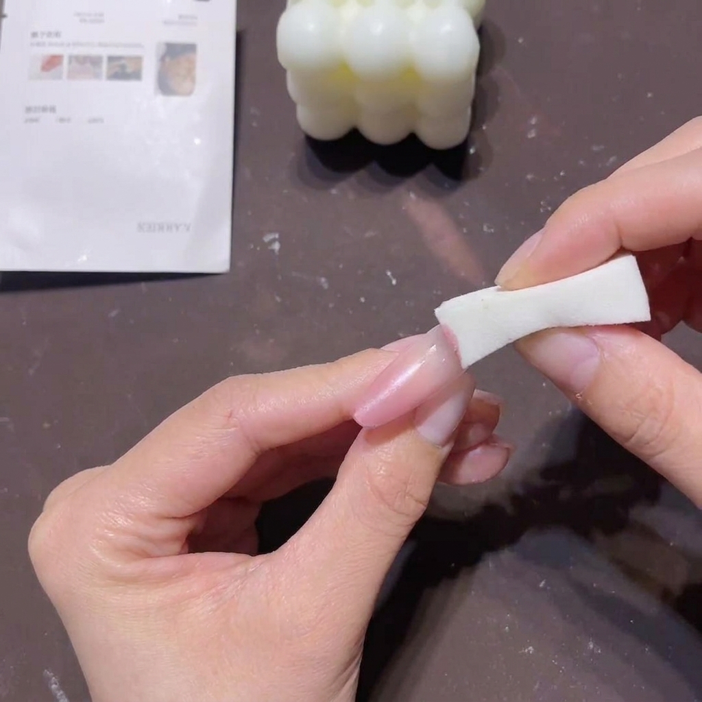 Gros plan dune main utilisant un bloc éponge blanc pour tamponner du gel pêche-rose sur le bout dun ongle long afin de créer un effet dégradé.