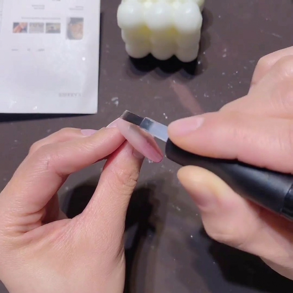 Un pinceau plat appliquant une couche lisse de base transparente sur un ongle en dégradé rose pour sceller la couleur.