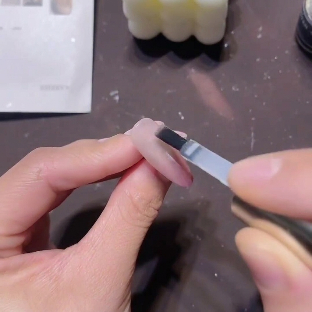 Un pinceau plat à gel appliquant un top coat de construction transparent épais sur un design dongle magnétique rose terminé.