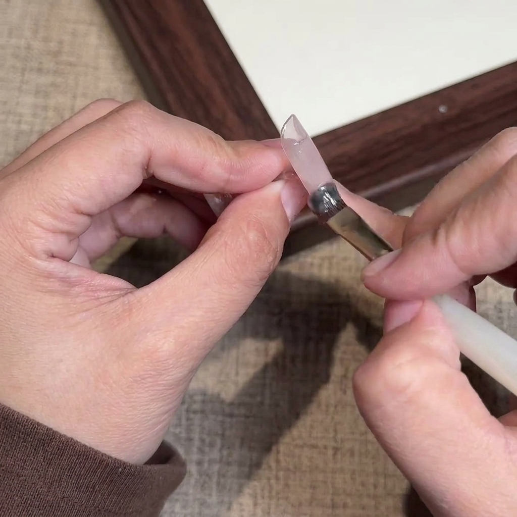 Gros plan dun pinceau appliquant un vernis gel nude rosé sur un ongle naturel.