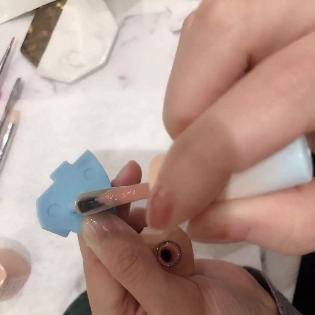 Gros plan dun pinceau appliquant un vernis gel rose nude transparent sur un ongle.