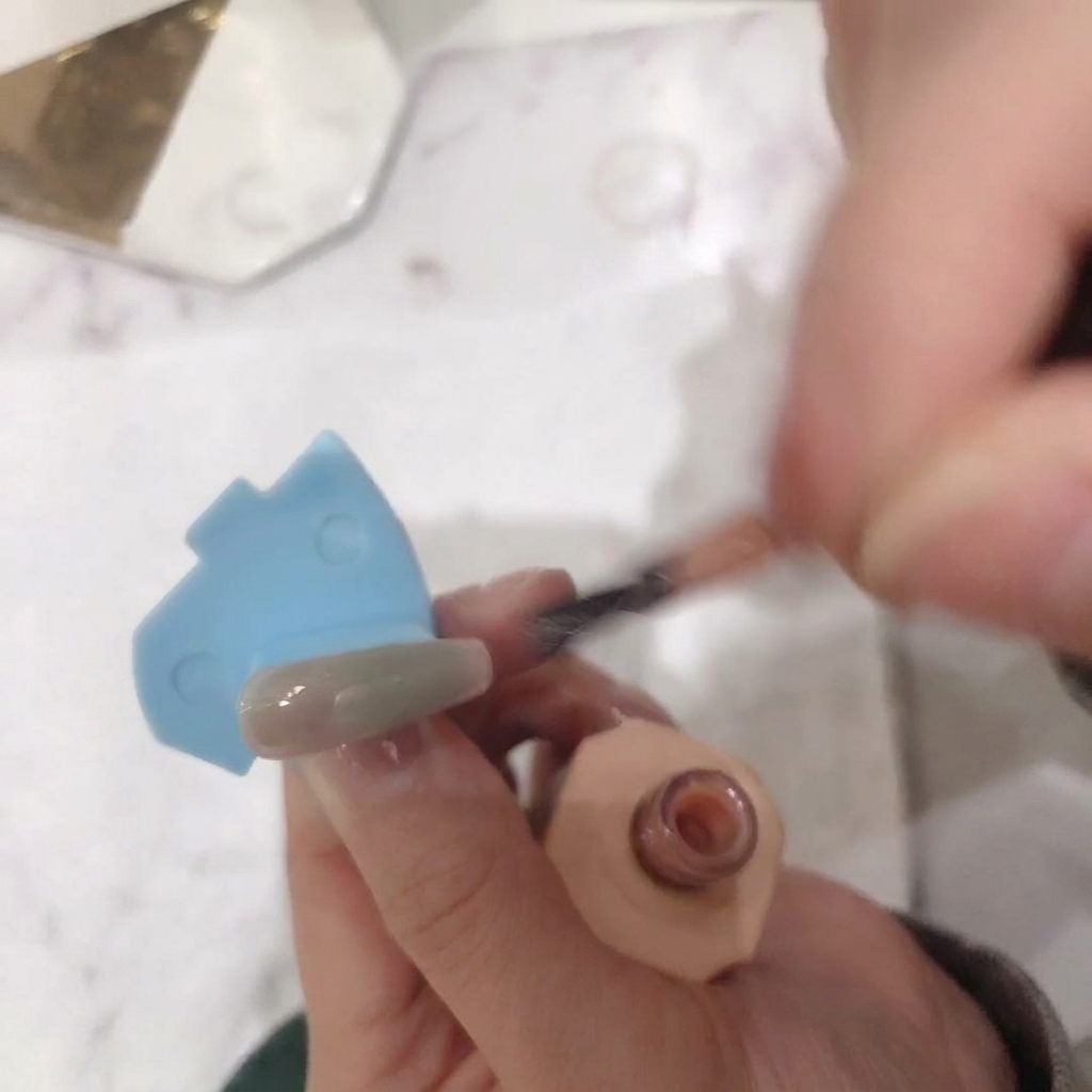 Vue rapprochée montrant la deuxième couche de vernis rose nude appliquée sur la surface de longle.
