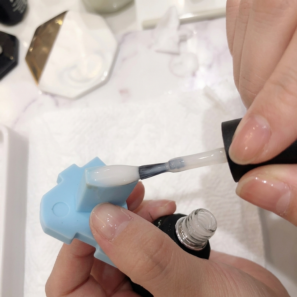 Gros plan dun pinceau appliquant une fine couche de vernis blanc laiteux sur un ongle ombré.