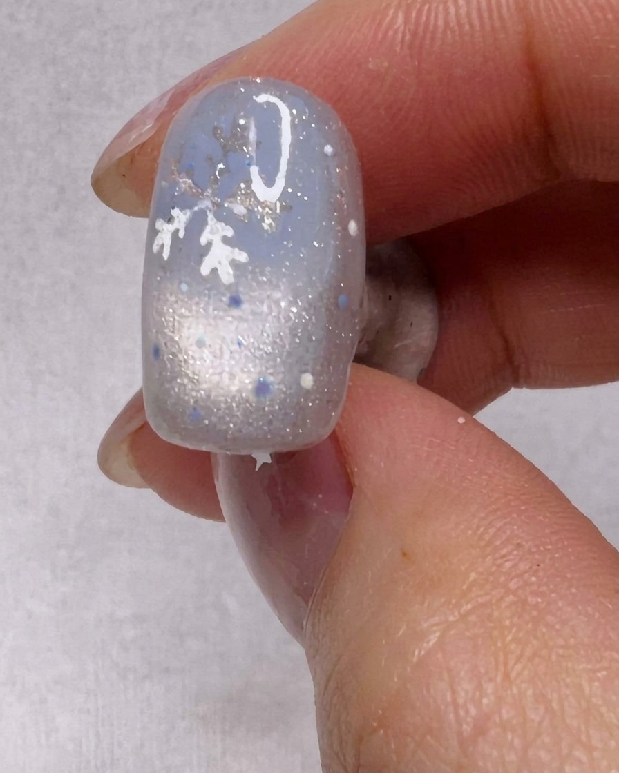 Un pinceau appliquant une couche de vernis gel argenté scintillant sur un ongle.