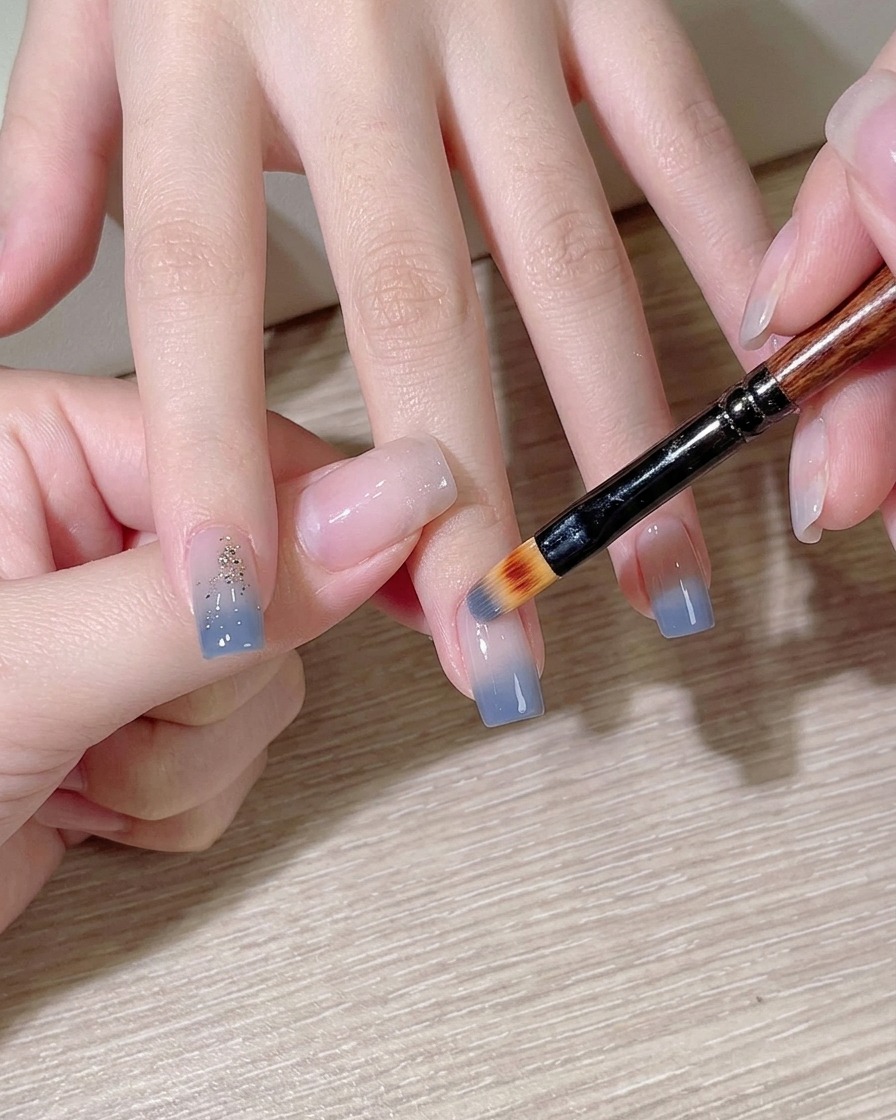 Une éponge de maquillage tamponnant du vernis bleu clair sur un ongle.