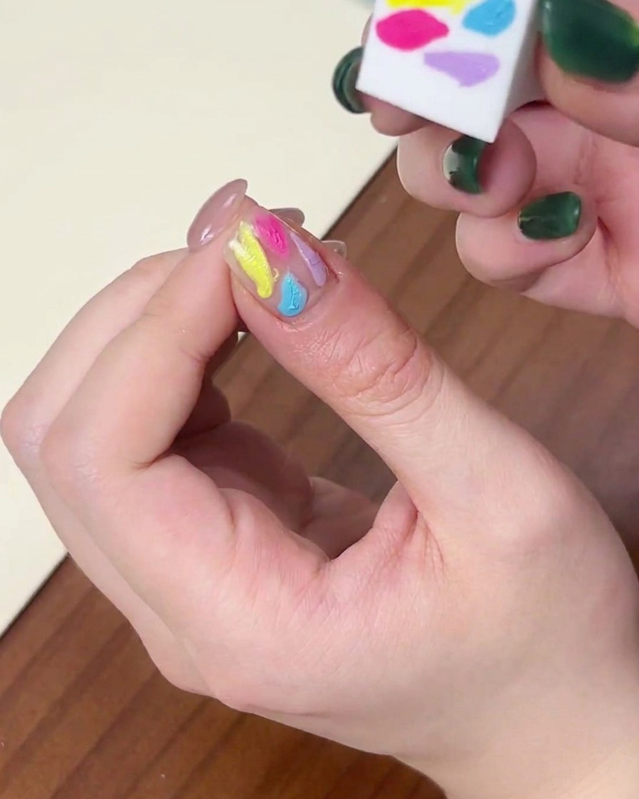 Vue rapprochée montrant le côté dune éponge utilisée pour fondre les points de vernis gel multicolores sur un ongle.