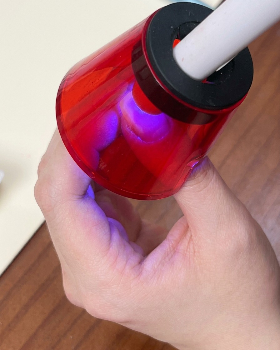 Un pinceau appliquant un vernis gel cat-eye blanc scintillant sur la base dégradée colorée.