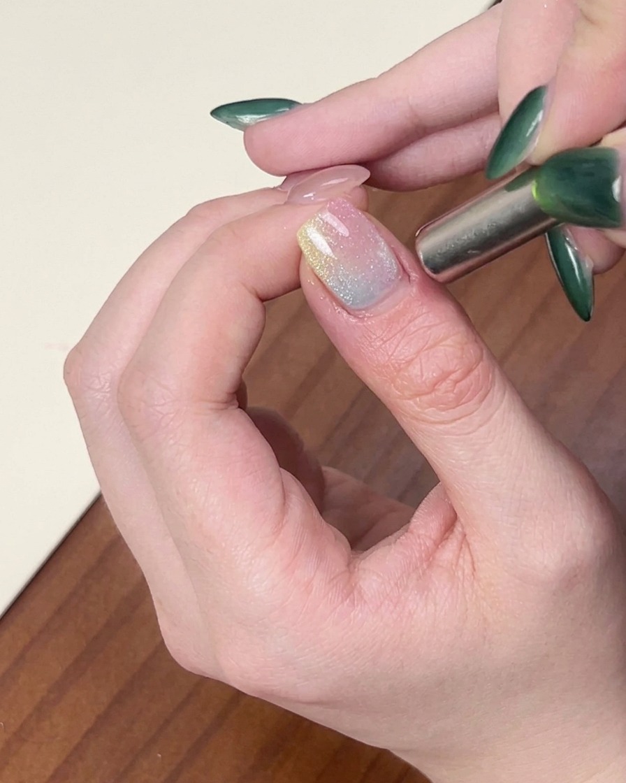 Un aimant cylindrique tenu près du bord dun ongle pour modeler le vernis gel cat-eye scintillant.