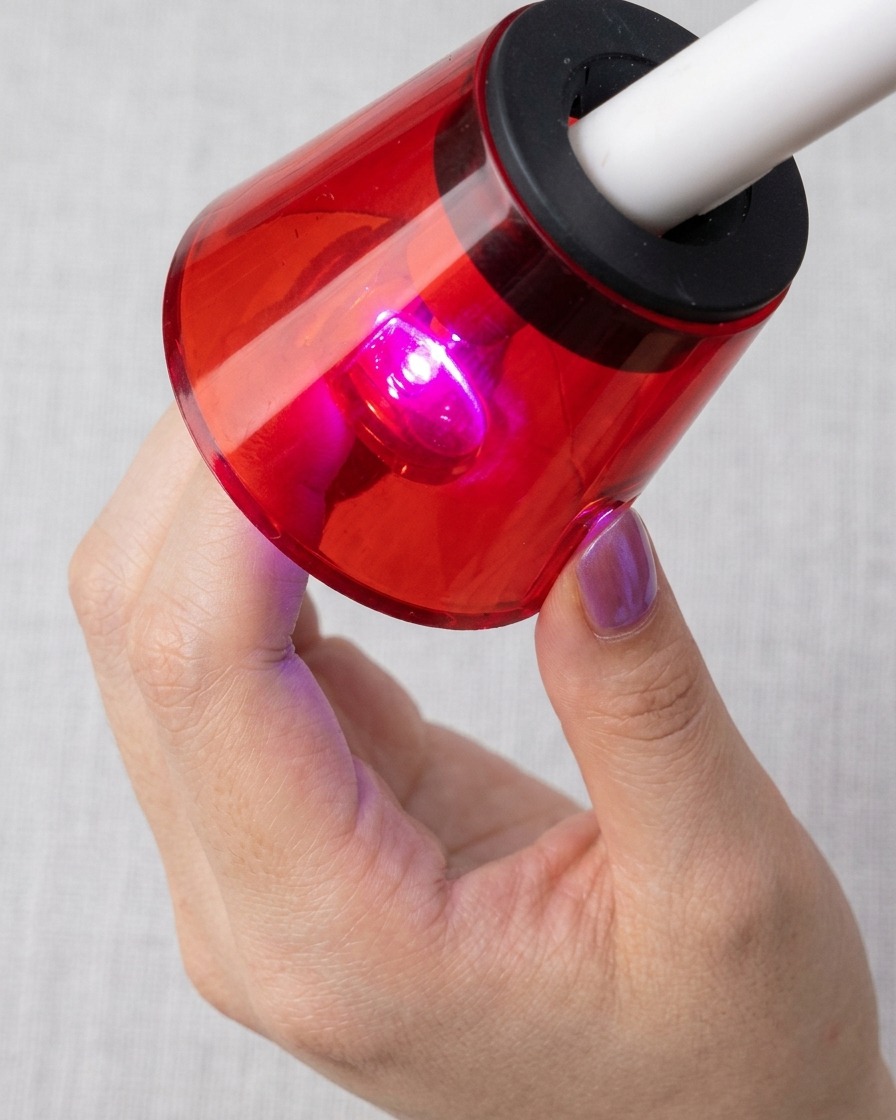 Un ongle placé sous une lampe UV/LED rouge, en train de catalyser avec les particules magnétiques cat-eye visibles.