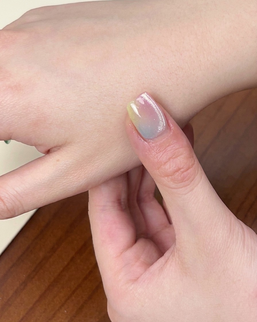 Gros plan dune main avec la manucure dégradée colorée terminée reposant sous une lampe à ongles UV/LED allumée.