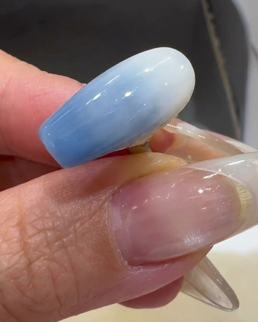 Un pinceau appliquant une fine couche de vernis gel blanc laiteux sur un tips dongle transparent.