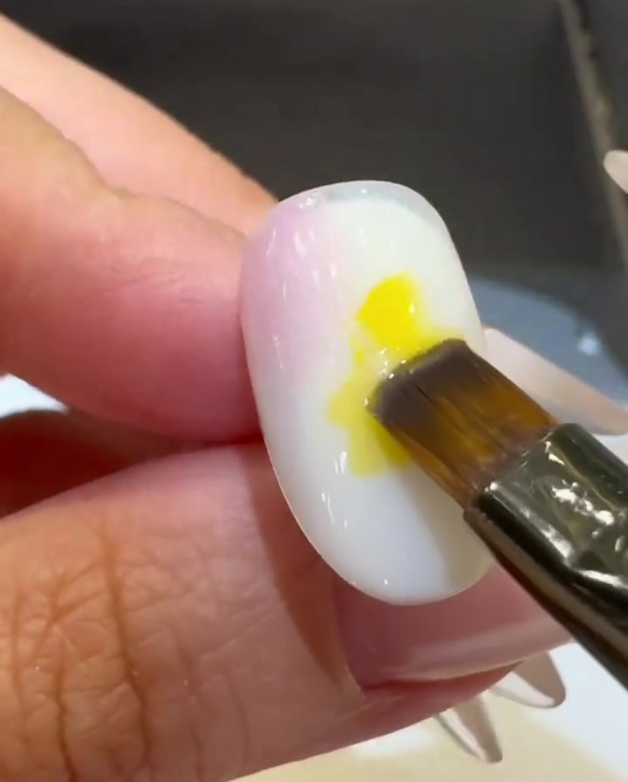 Un pinceau plat déposant une goutte de vernis gel jaune vif au centre de longle.