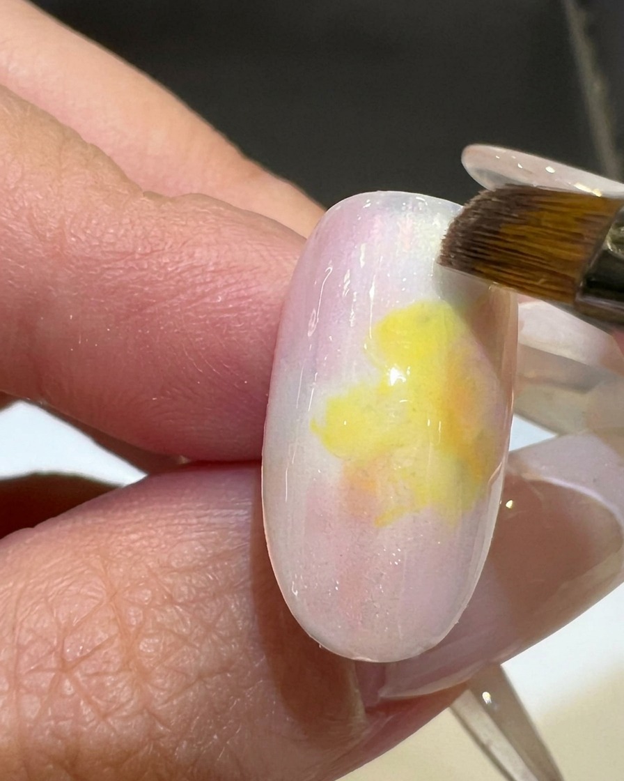 Un pinceau plat lissant le dégradé entre le vernis gel rose et jaune sur un tips dongle.