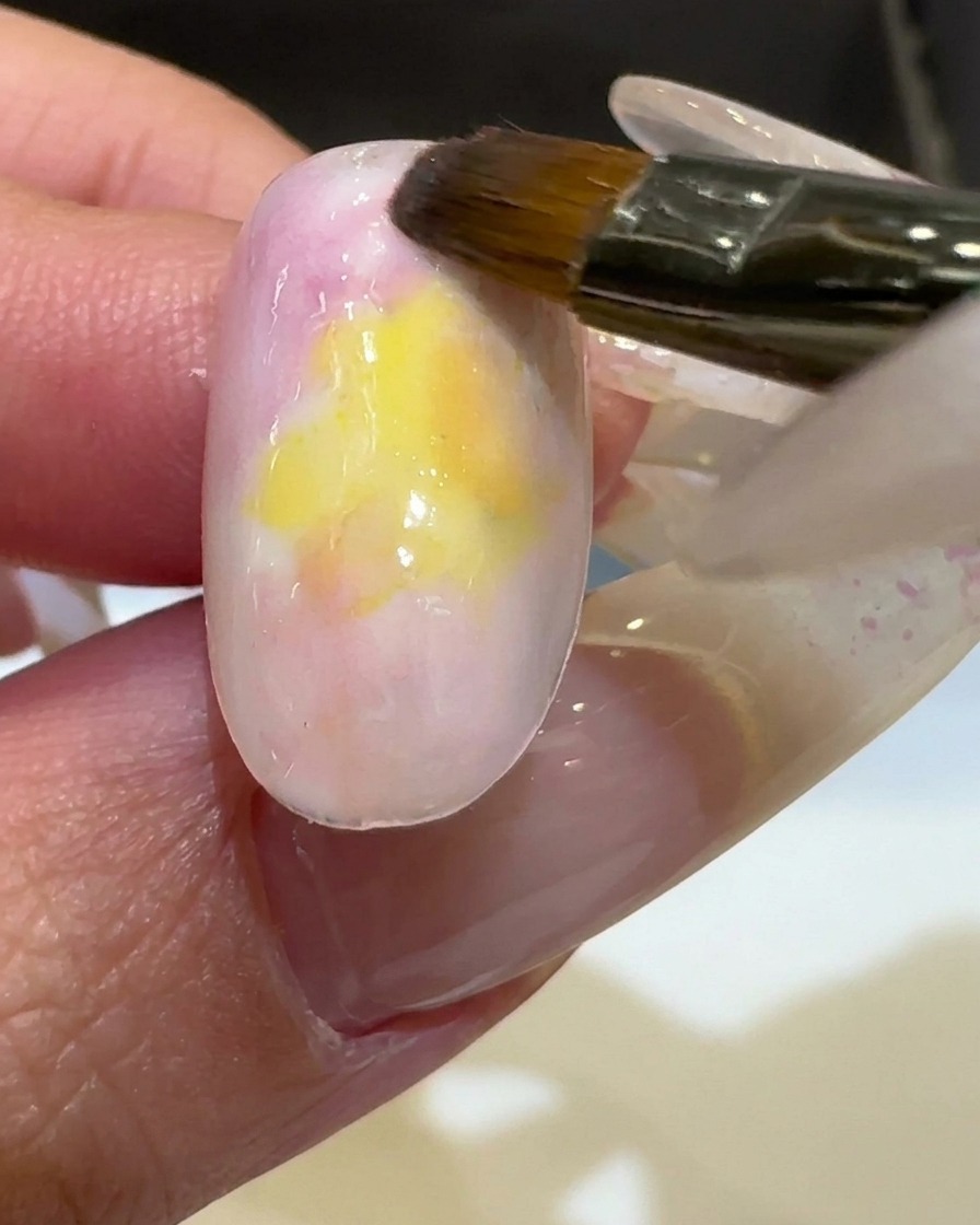 Un pinceau appliquant un vernis gel jaune vibrant au centre dun ongle, se mélangeant aux couleurs existantes.