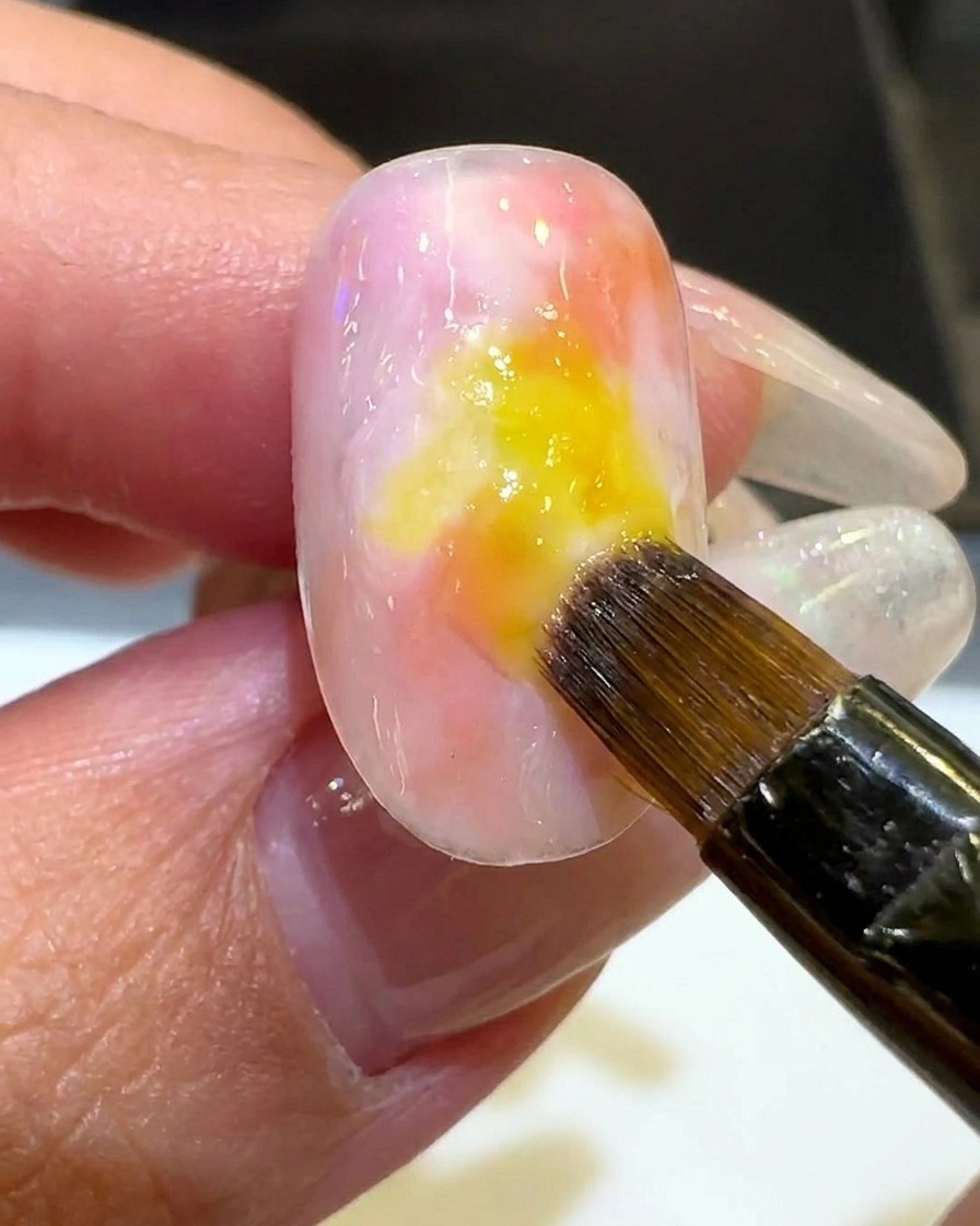 Un pinceau appliquant une fine couche diaphane de vernis blanc laiteux autour du périmètre du dégradé coucher de soleil coloré.
