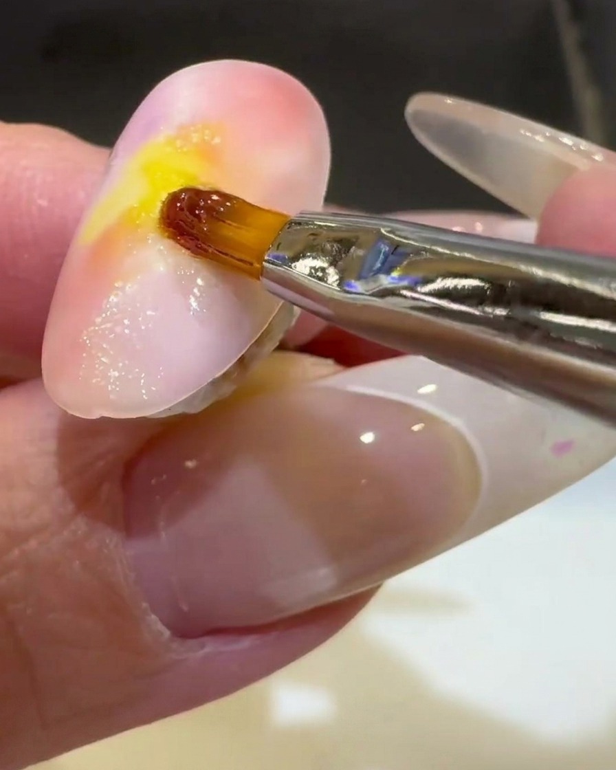 Un pinceau liner fin finissant une vague de gel 3D transparent sur la moitié inférieure dun ongle couleur coucher de soleil.