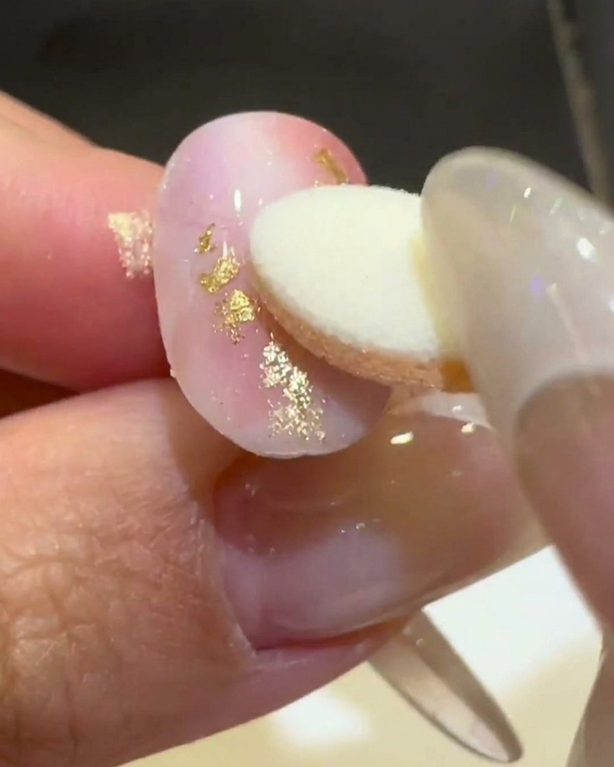 Un applicateur éponge frottant de la poudre chrome aurora dorée sur une ligne ondulée 3D en relief sur un ongle mat rose et blanc.