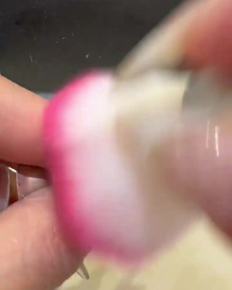 Un pinceau dépoussiéreur rose et duveteux balayant un ongle pour enlever lexcès de poudre chrome dorée.