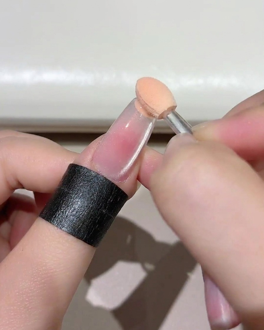 Gros plan dune éponge appliquant du gel rose sur le bord libre dun ongle.