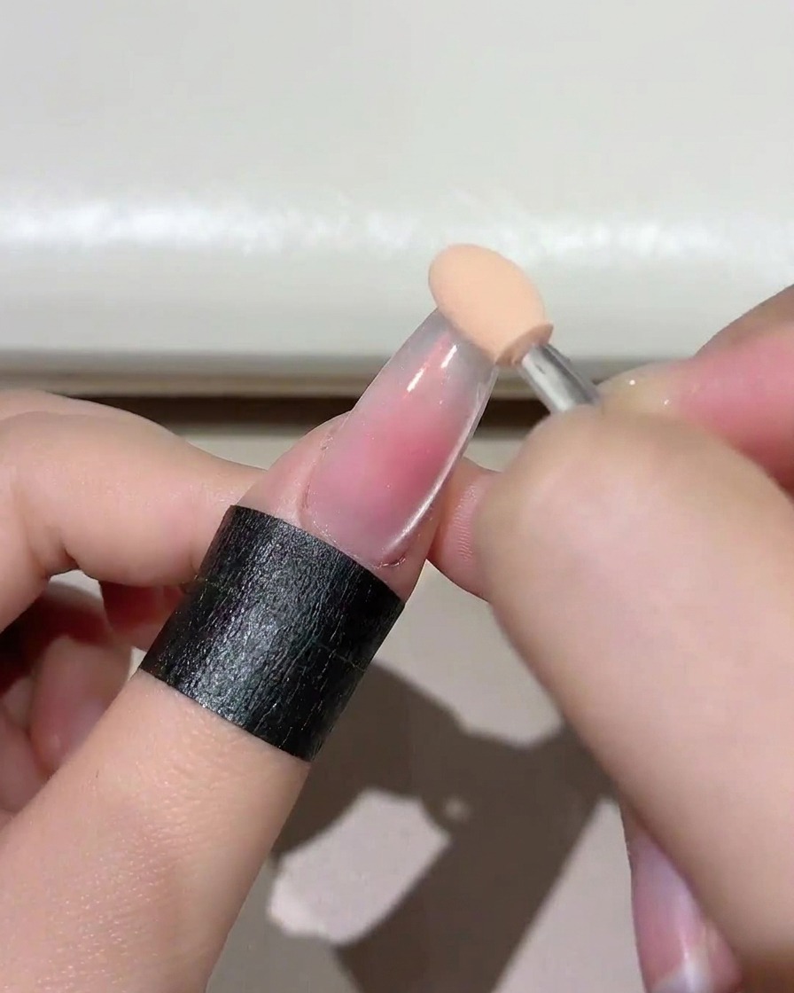 Gros plan dune éponge appliquant un gel rose blush sur le bout de longle.