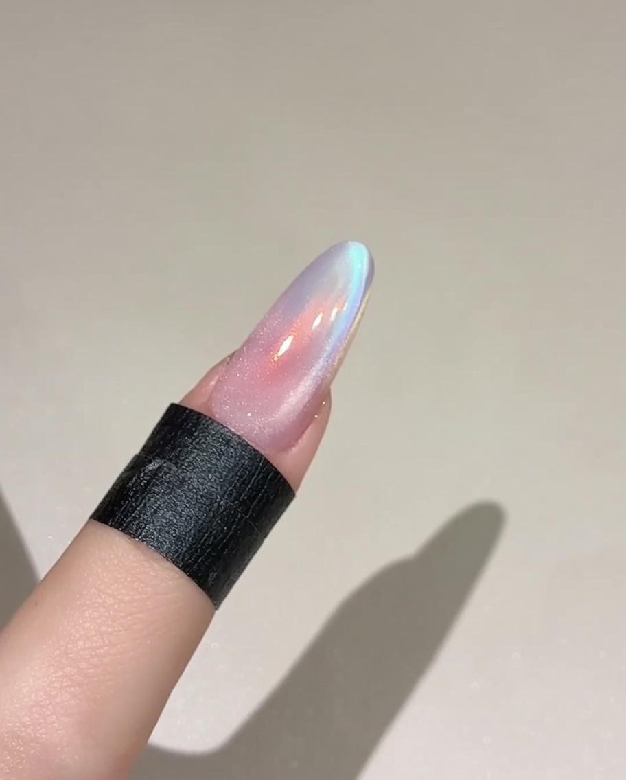 Un pinceau appliquant un gel cat eye translucide sur un ongle coloré.