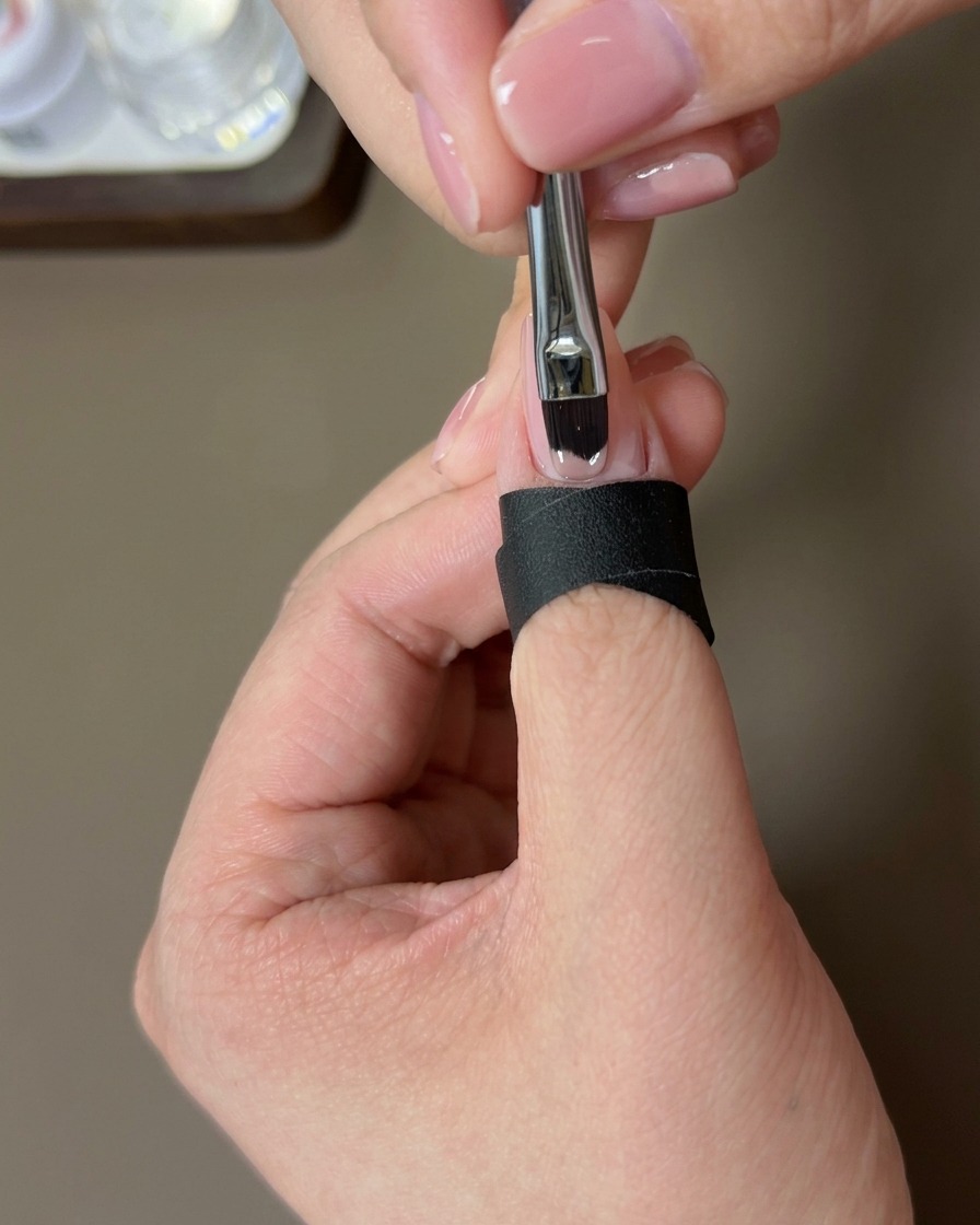Un pinceau appliquant une couche de vernis gel nude sur longle naturel.