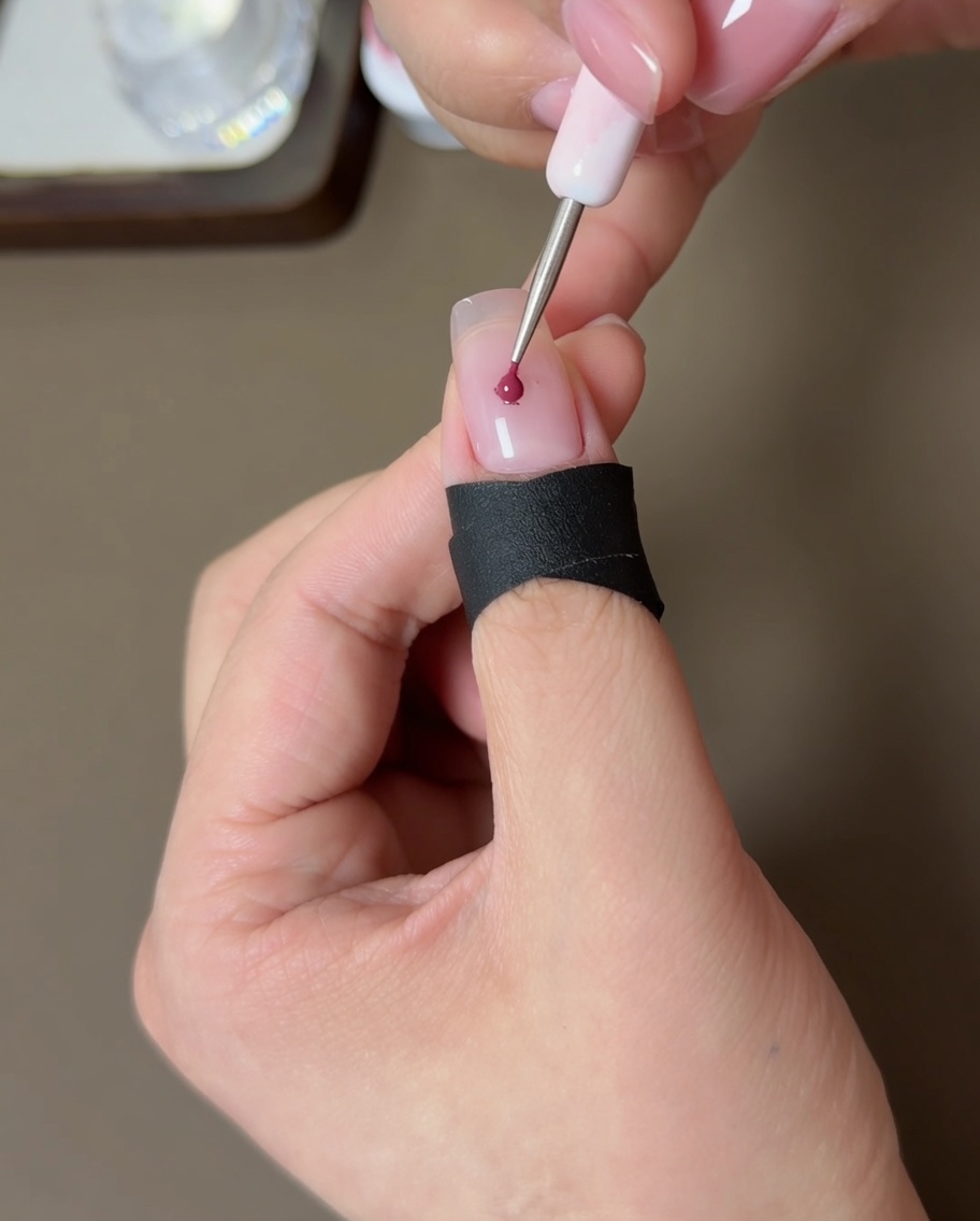 Un petit outil appliquant un point de gel pêche au centre dun ongle nude.