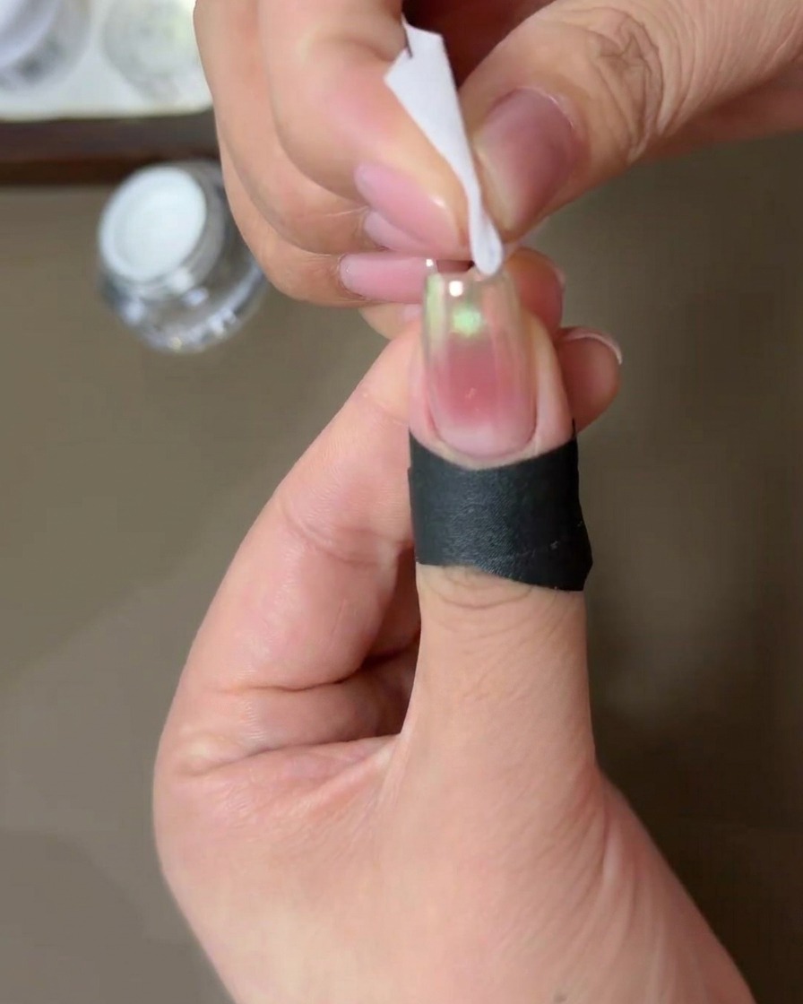 Une personne utilisant une lingette non pelucheuse imbibée dalcool pour nettoyer les bords dun ongle recouvert de poudre chrome aurore.