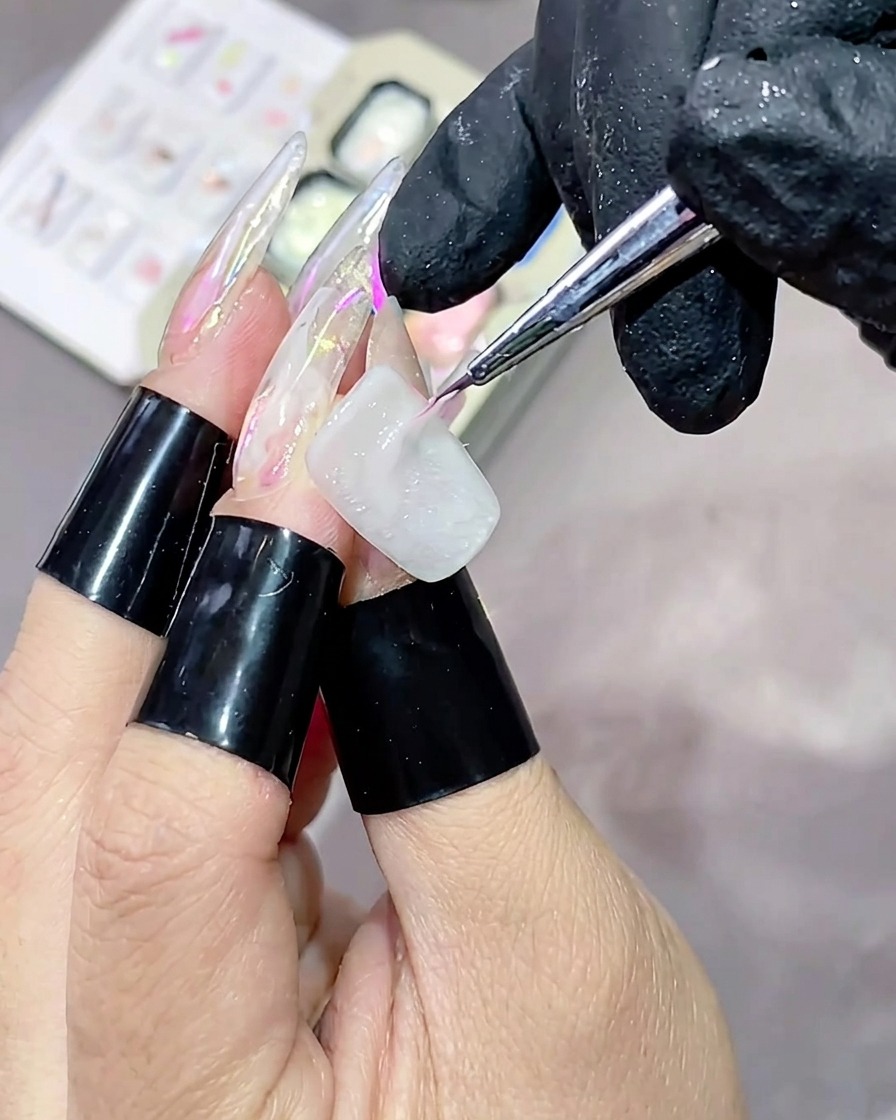 Un pinceau fin appliquant un trait de gel texturé rose ultra-brillant horizontalement sur un ongle peint en blanc.
