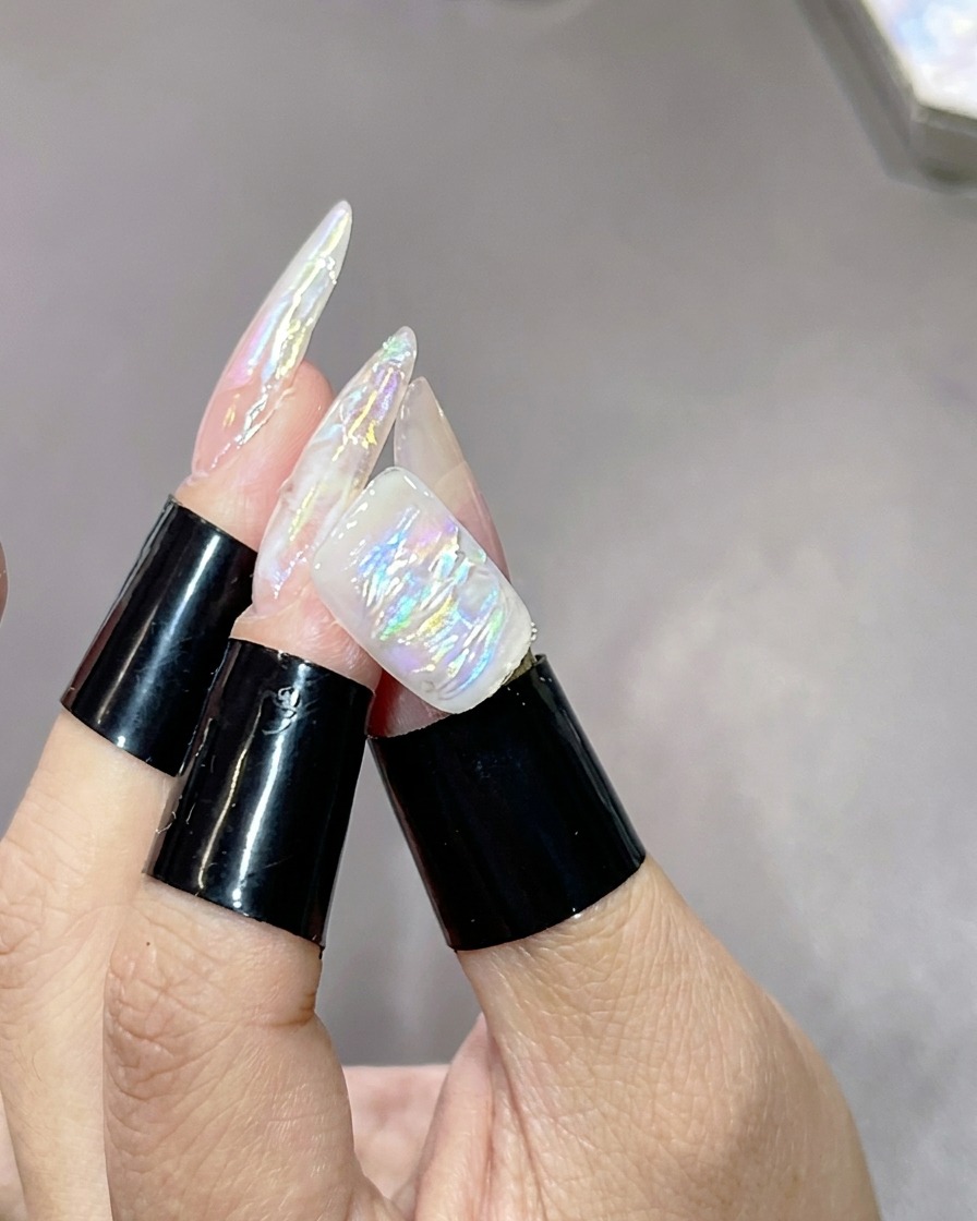 Une main avec des ongles texturés et marbrés posée dans une lampe UV pour catalyser la couche de lumière.