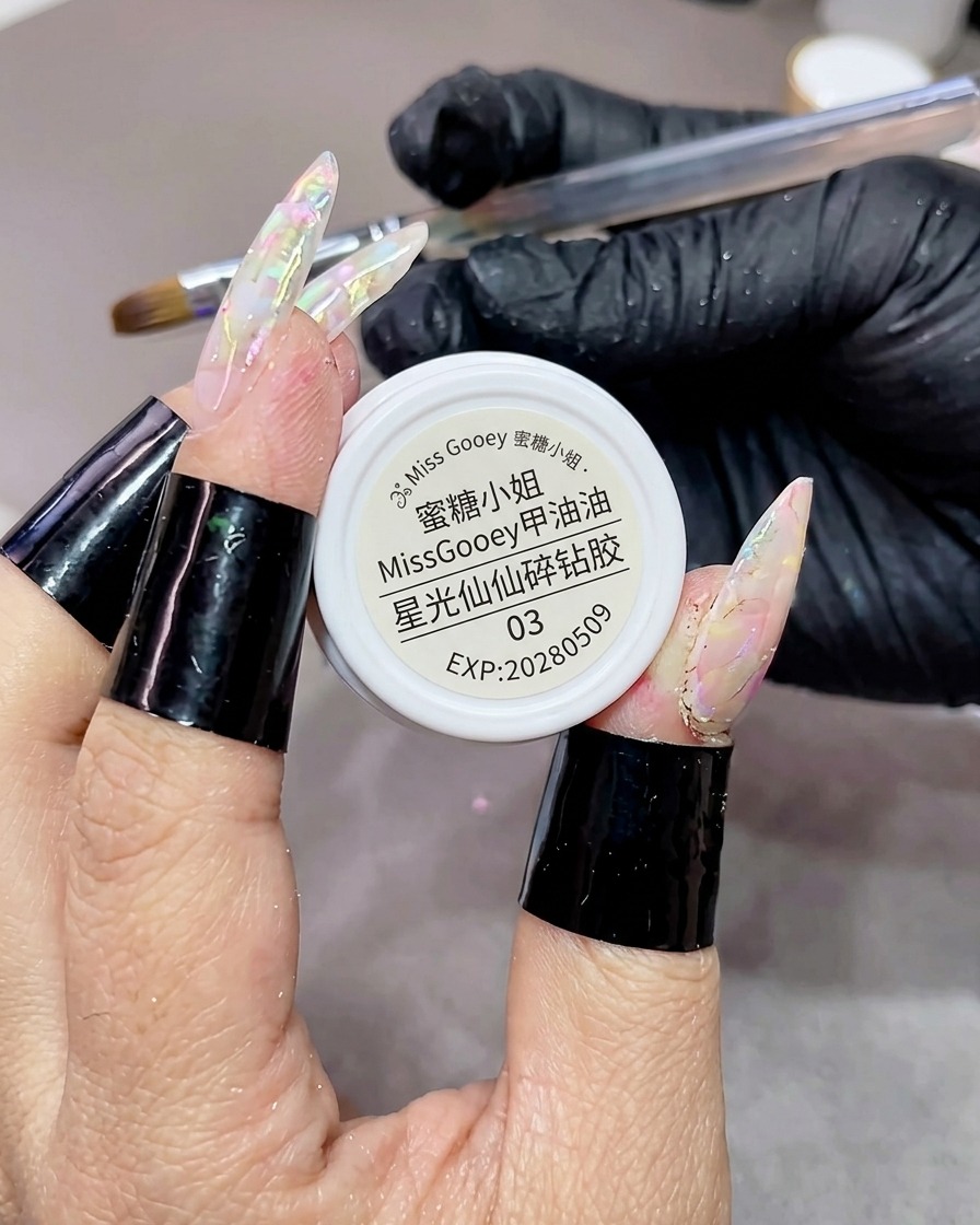Un pinceau appliquant un gel à paillettes en forme détoiles sur un ongle en gel texturé et marbré en effectuant des mouvements en zigzag.