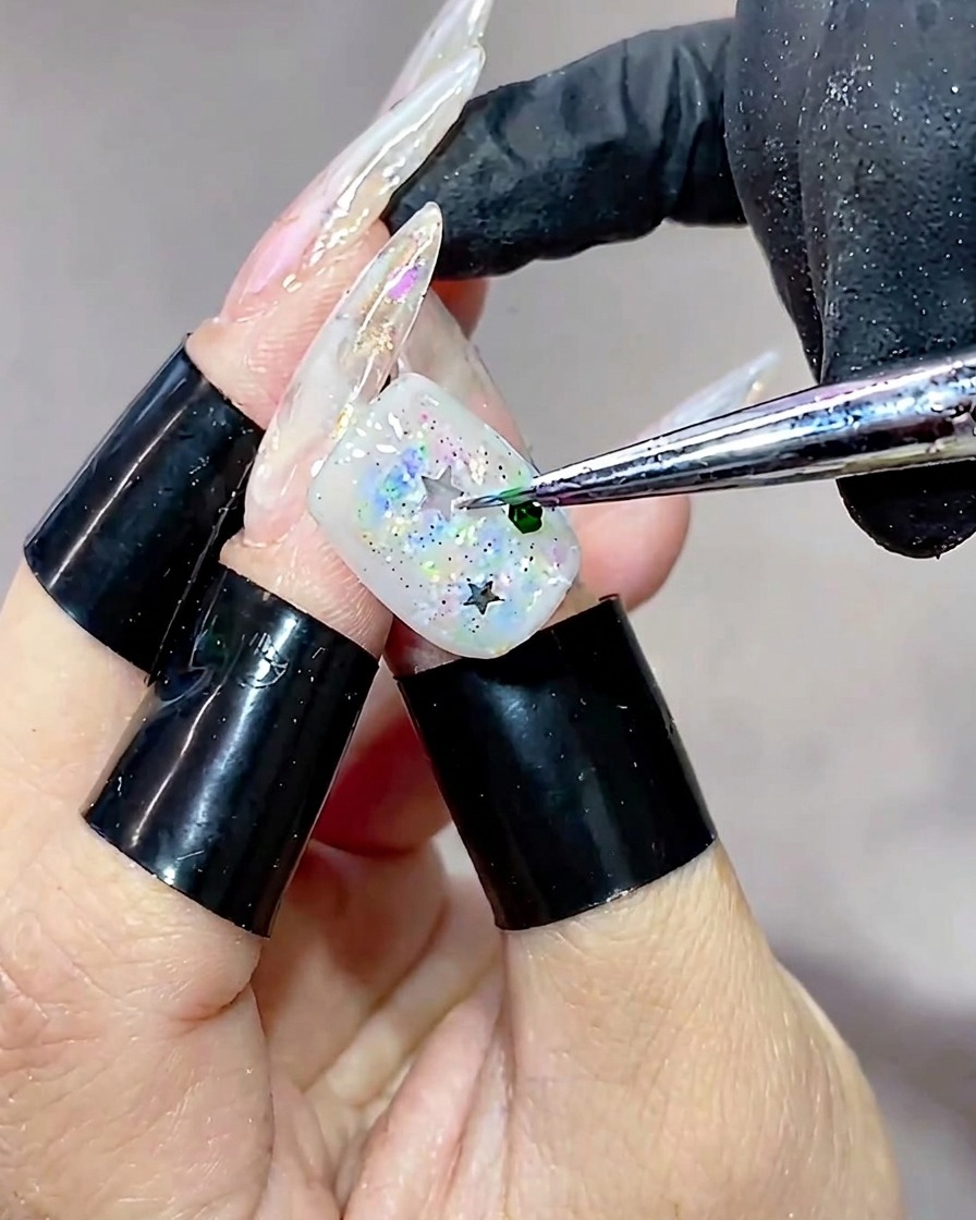 Vue de très près dun outil déposant un petit sequin vert hexagonal sur la surface dun ongle déjà parsemé détoiles pailletées.