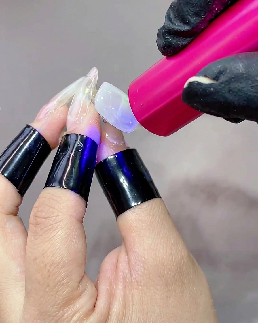 Une main placée sous une lampe UV portable, la surface de longle brillant pendant que le gel se catalyse.