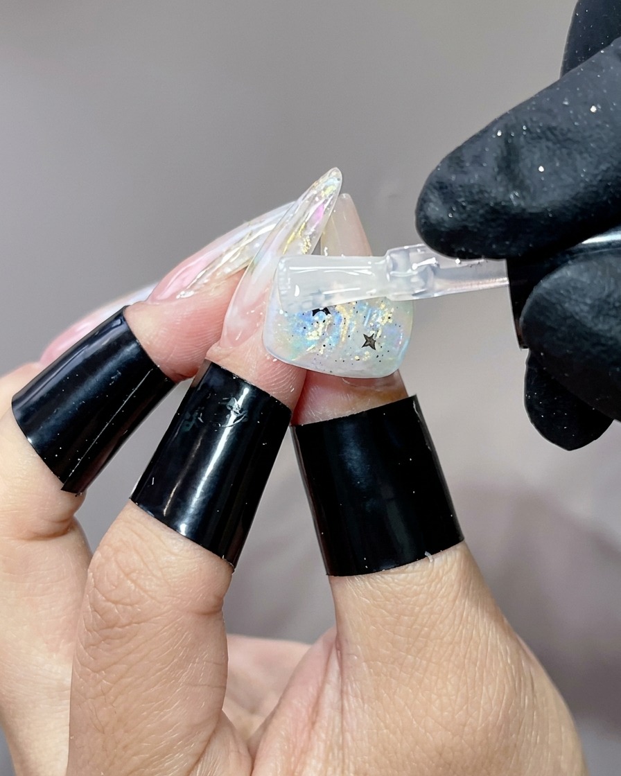 Un pinceau appliquant une dernière couche de finition brillante sur un motif dongle avec des paillettes étoilées.