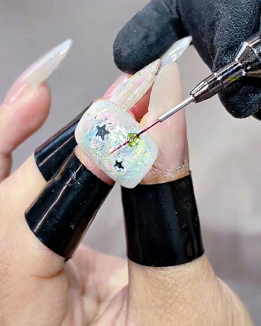 Plan très rapproché montrant un pinceau fin déposant une goutte ronde de gel transparent et dur sur un sequin vert.