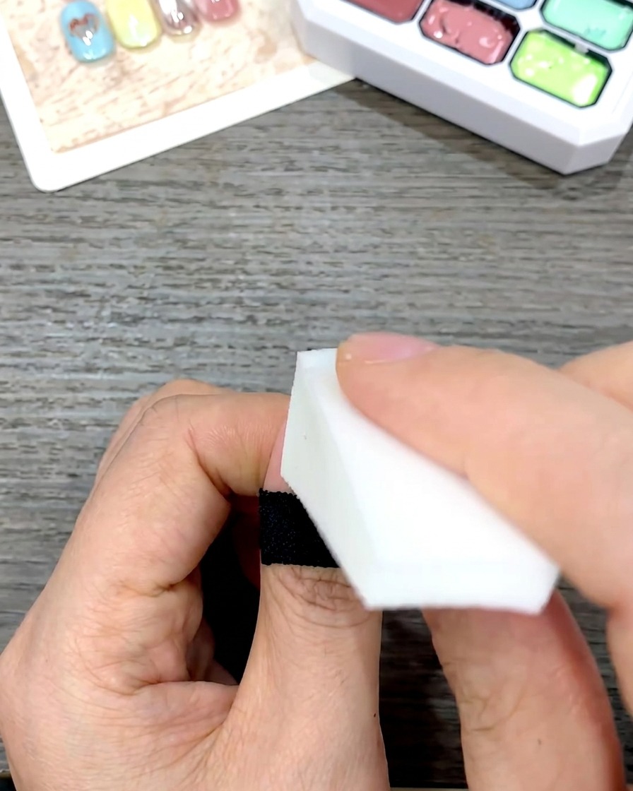 Une main utilisant une éponge en mousse triangulaire blanche pour tapoter et mélanger doucement le vernis gel jaune vers le bas de longle.