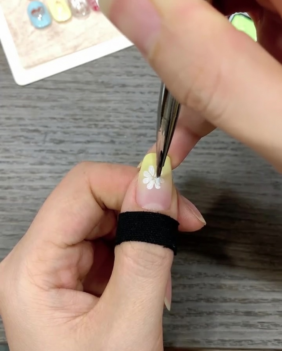 Gros plan dun ongle décoré au pinceau fin avec un petit point jaune vif au centre dune marguerite blanche.