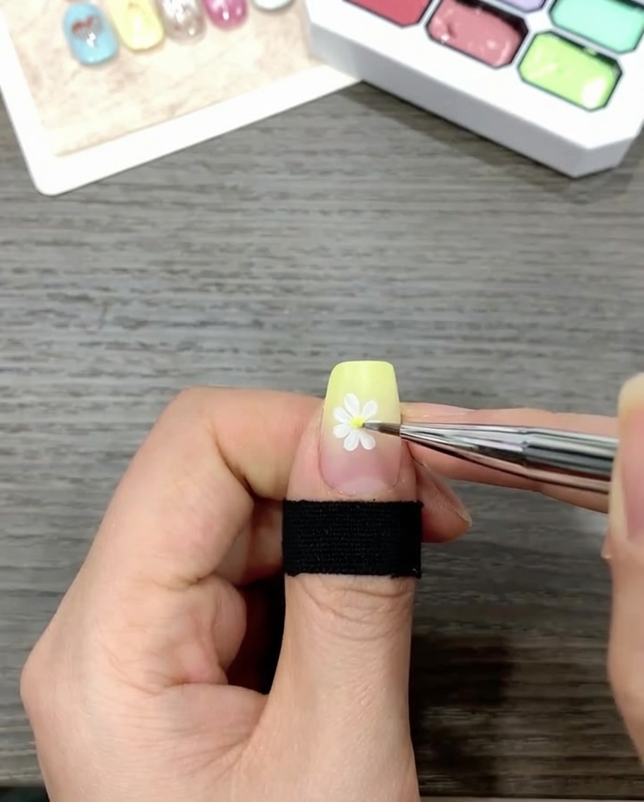 Un pinceau appliquant un top coat transparent brillant sur un ongle décoré dune marguerite sur fond dégradé.