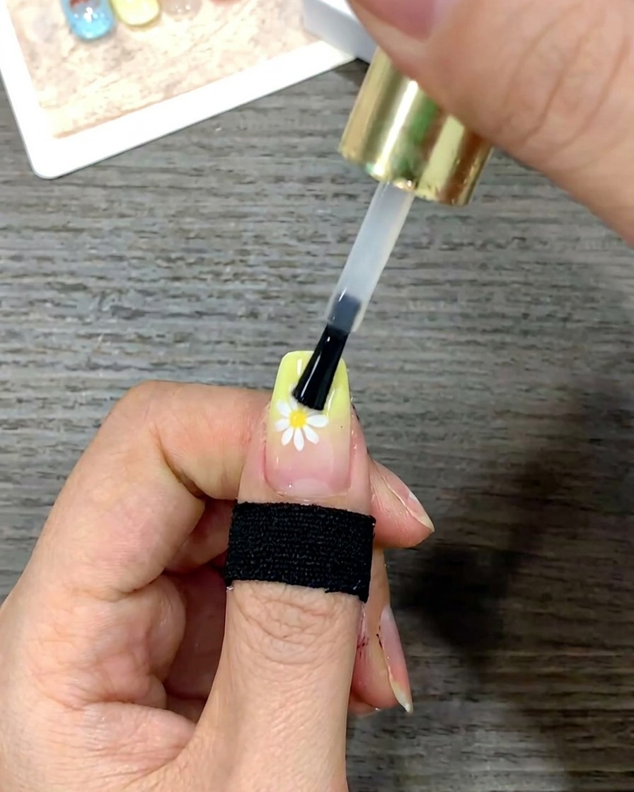 Gros plan dun pinceau lissant une couche de top coat brillant sur toute la surface de longle.