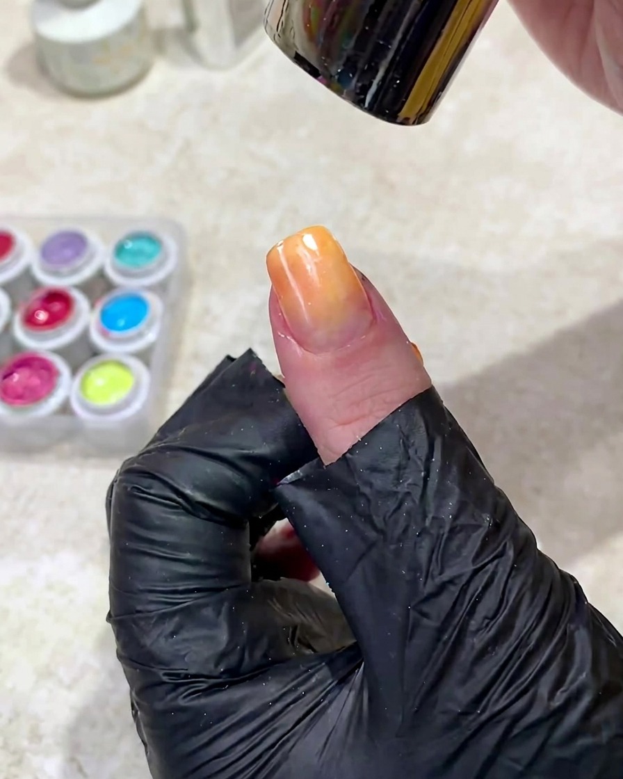 Une main positionnée sous une lampe à ongles UV pour catalyser le gel dégradé fraîchement appliqué.