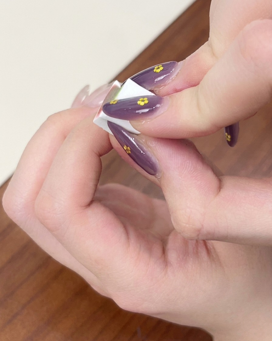 Des doigts tenant une petite éponge de maquillage blanche, tapotant et estompant le vernis gel bleu pour créer un effet ombré sur un ongle.