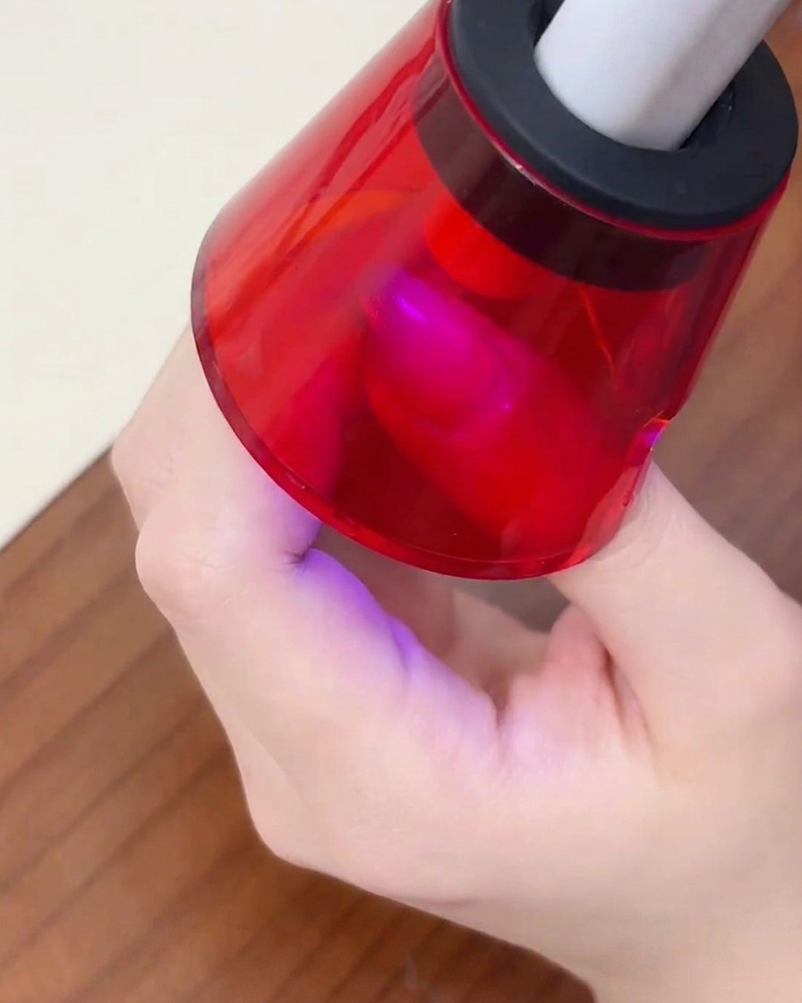 Un doigt posé sous une mini lampe UV portable rouge pour catalyser le vernis gel.