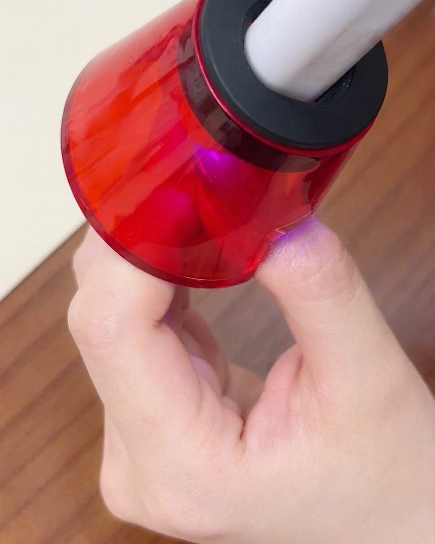 Gros plan dun doigt placé sous une mini lampe UV/LED portable rouge pour la catalyse finale.