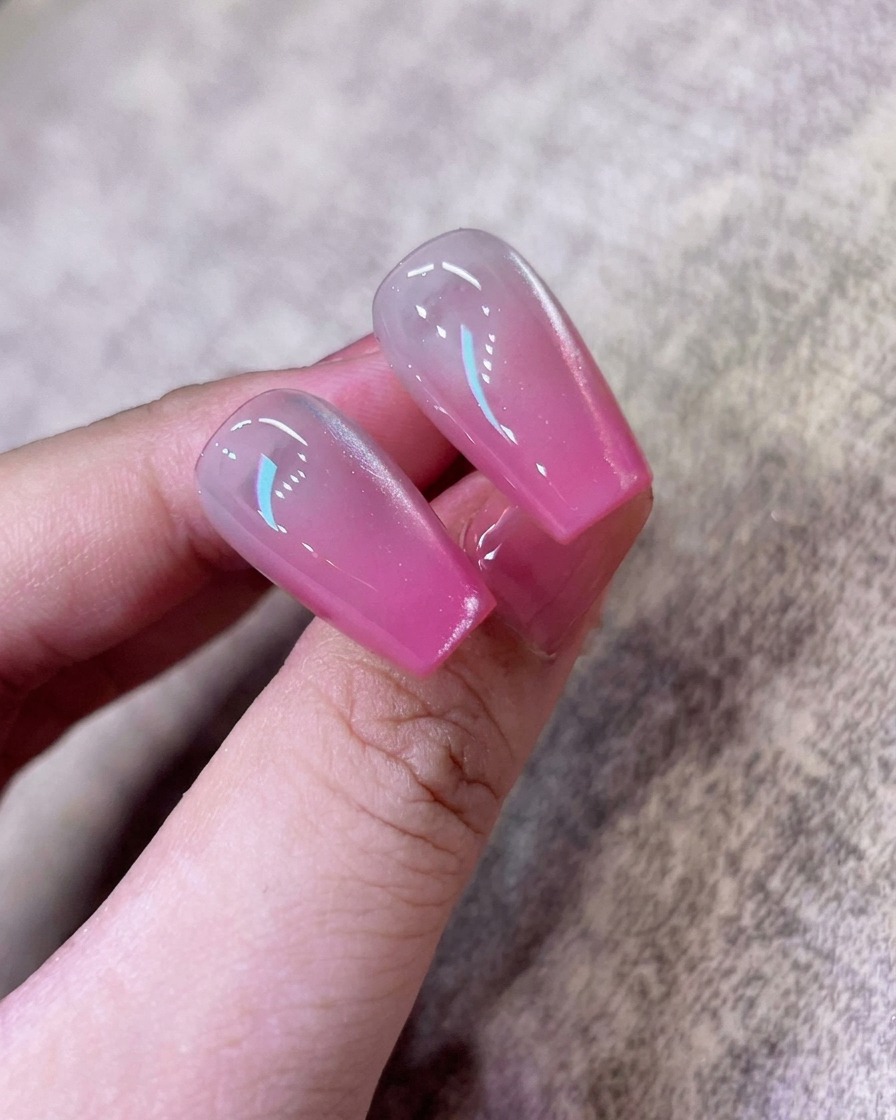Un pinceau appliquant une couche de gel cat-eye blanc scintillant sur longle ombré rose existant.